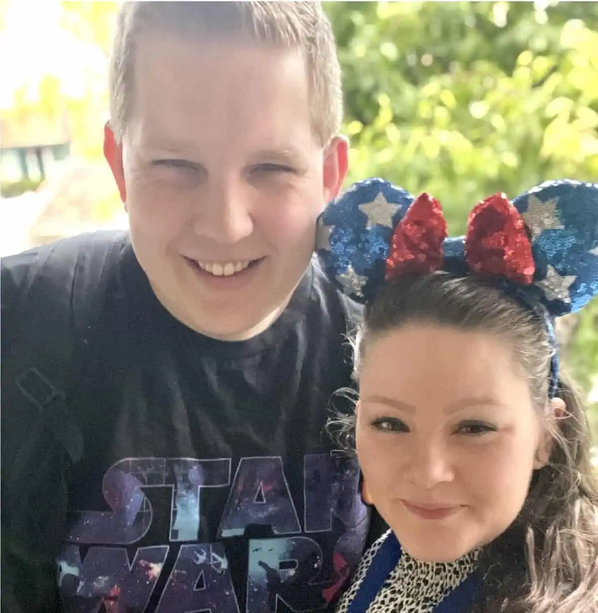 Photo of Natasha and her husband, smiling together — Natasha is wearing blue Minnie ears. Happy clients who shared a testimonial about their Disney experience.