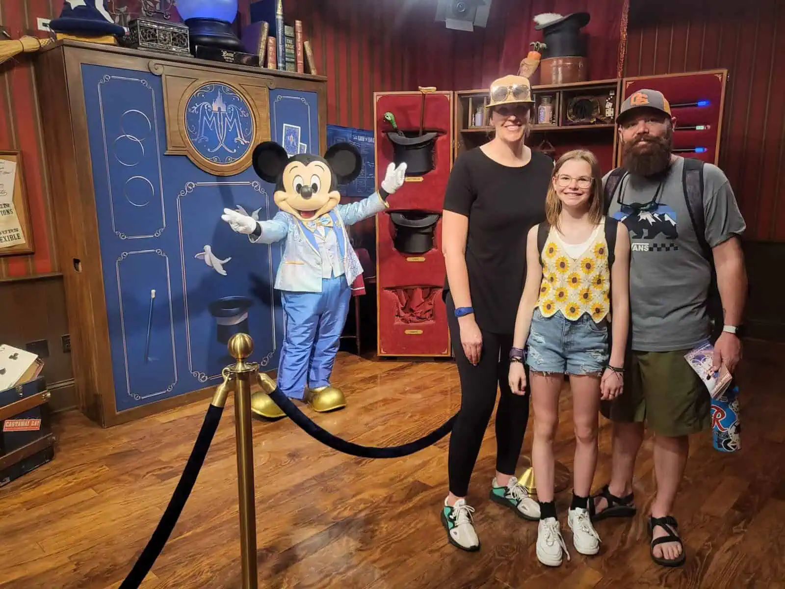 Photo of Richard B. and his family — mom, dad, and daughter standing together with Mickey Mouse in the background, arms outstretched during a socially distanced Disney visit.