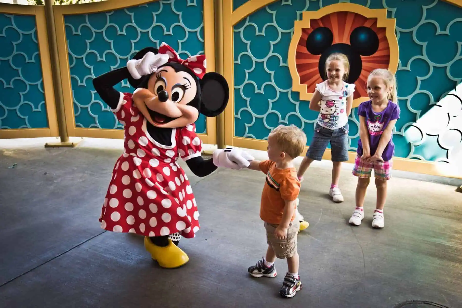 Photo of Nathan W.’s two-year-old son holding Minnie Mouse’s hands as she kneels and playfully holds her hand to her forehead, as if he just proposed — two older girls stand in the background laughing.