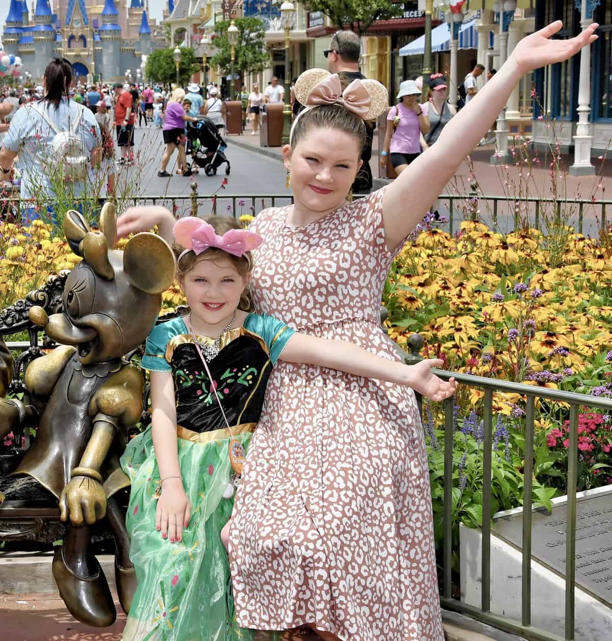 Photo of Natasha and her daughter at Magic Kingdom sitting next to a Minnie Mouse statue, smiling with their arms spread out — happy clients who shared a testimonial about their Disney trip.