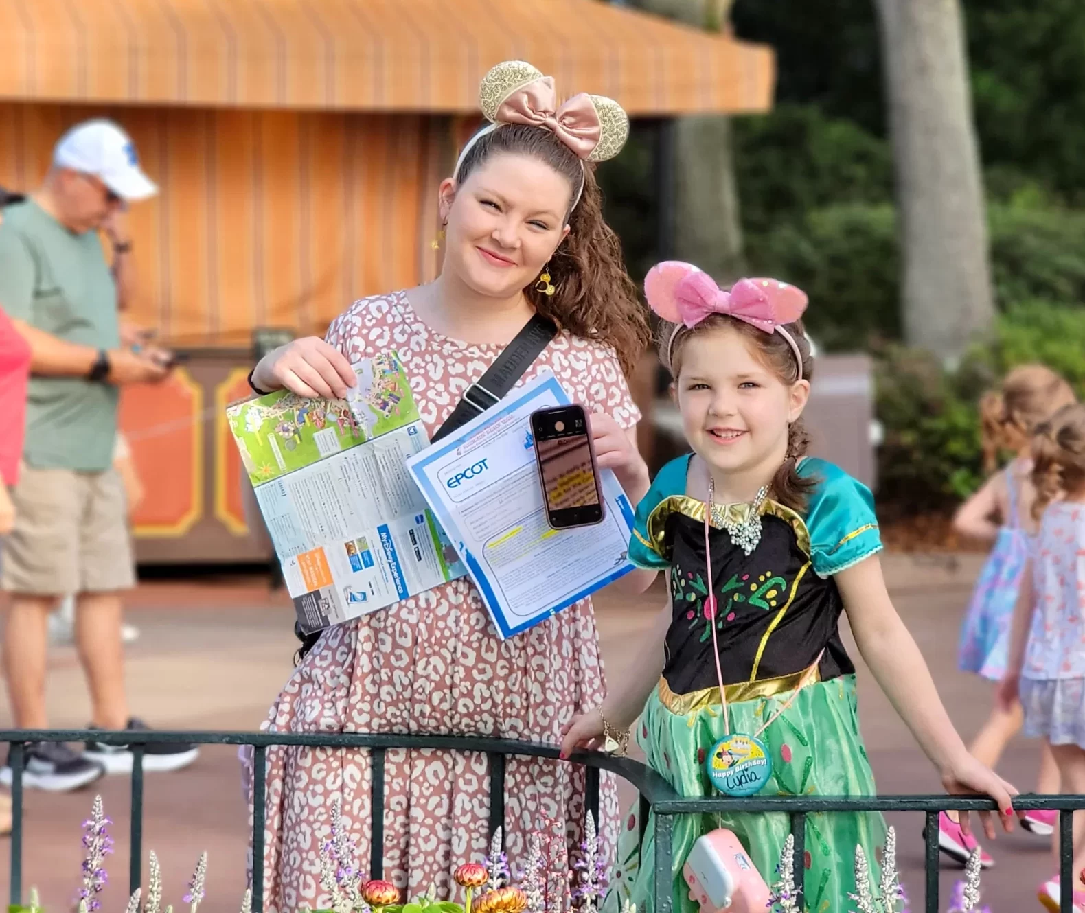 Mom and daughter smiling in EPCOT, wearing Minnie ears and holding a park map and their personalized Disney itinerary, which the mom called her ‘lifeline’