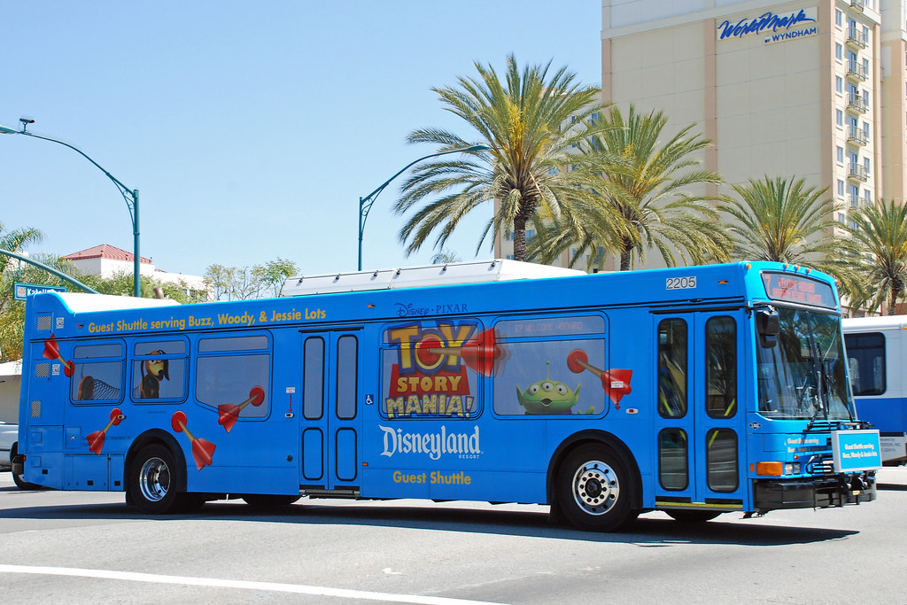 Blue Disneyland bus that says Toy Story with Pixar decorations on it driving past palm trees and a hotel.