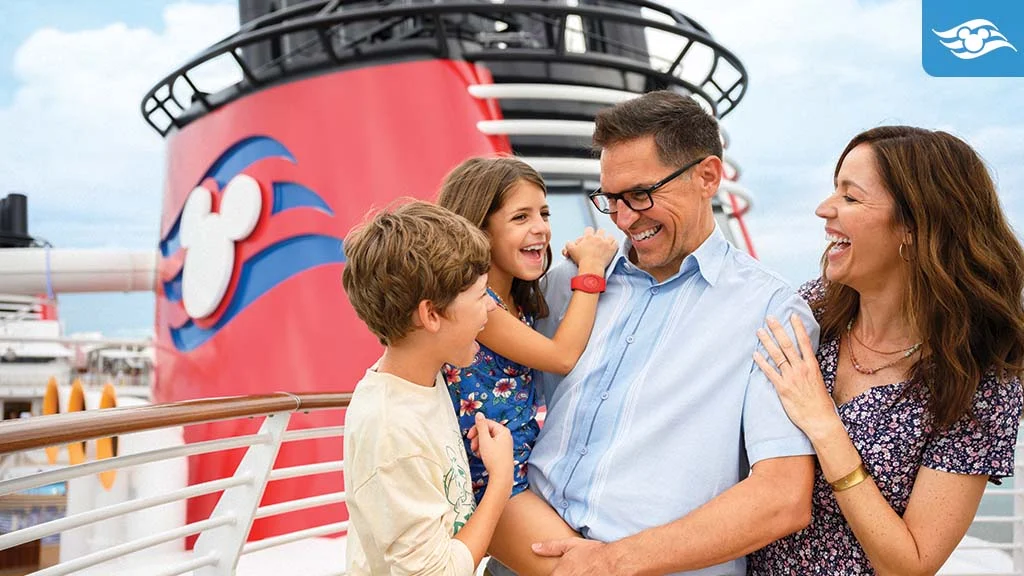 Smiling family on a cruise with the red funnel from a Disney cruise ship in the background.