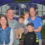 Will S. Family smiling in front of Floral Mickey in Disneyland California